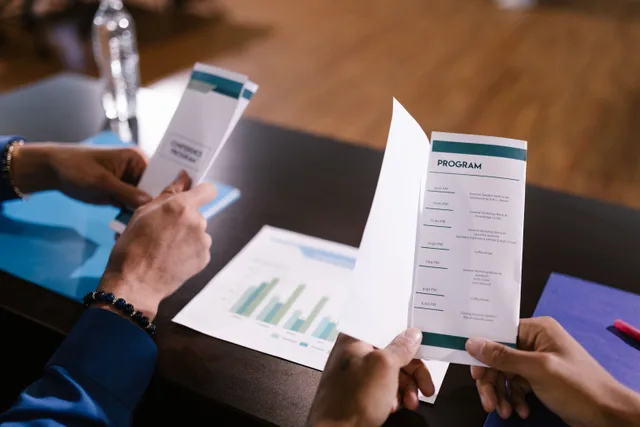 Hands examine program guide in a corporate meeting setting, highlighting agenda details. How to vet nonprofit fundraising campaign agencies: what to ask and check